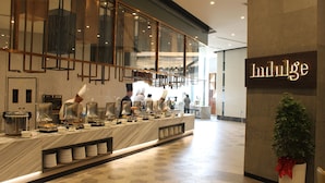 A buffet area with a marble counter, multiple serving stations, and a sign reading "Indulge". - M World Hotel (Petaling Jaya)