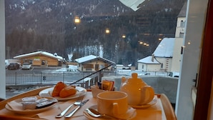 A dining table with a meal set, a view of a snowy mountain, and a building with a clock. - Hotel Piz Boè (Mazzin)