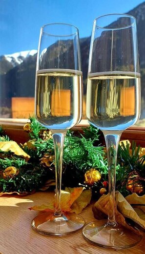 Twee champagneglazen met een heldere vloeistof, geplaatst op een houten oppervlak met een decoratieve compositie van kegeltjes en groen.