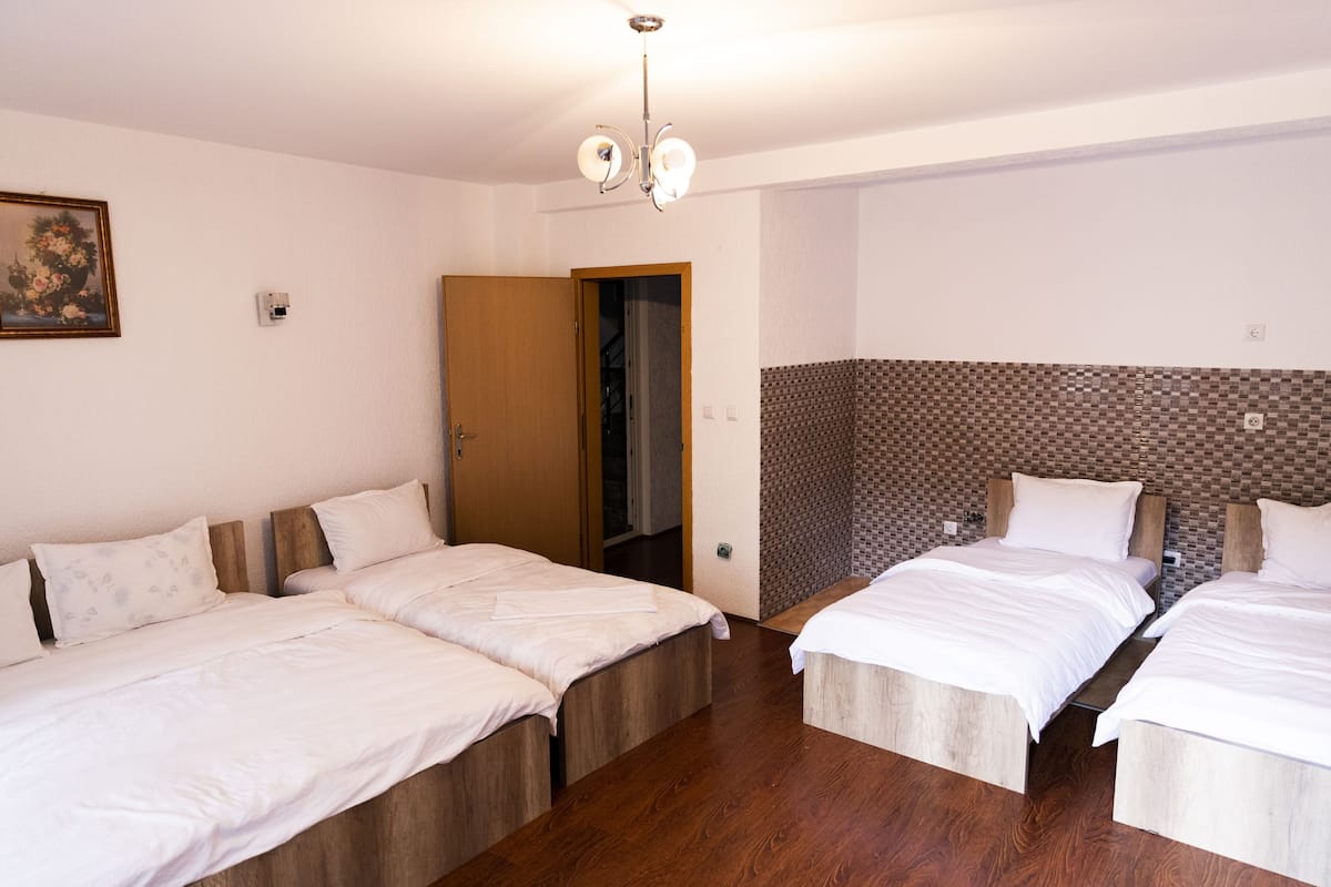 Ein Hotelzimmer mit zwei Einzelbetten, Holzboden, einer Wand mit Fliesen und einer Tür zum Badezimmer sowie einer Deckenleuchte.