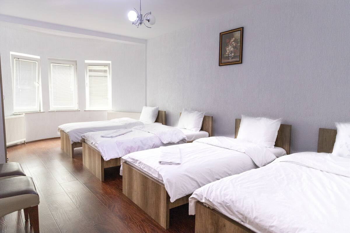 Ein Hotelzimmer mit drei hölzernen Betten, weißer Bettwäsche, einer Bank und einem Bild an der Wand.
