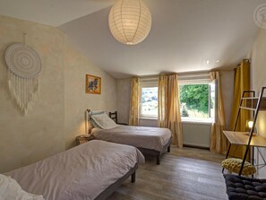Ein Schlafzimmer mit zwei Betten, einer Hängelampe, einem Fenster mit Vorhängen und einem Nachttisch mit Lampe.