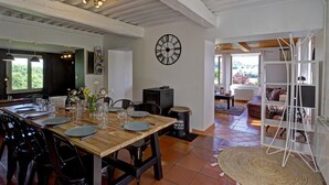 Zona de dinar amb taula de fusta preparada per a quatre persones, rellotge negre a la paret i vista a l'exterior a través d'una finestra.