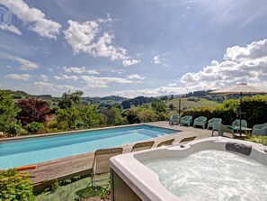 Une piscine avec un jacuzzi et un espace salon extérieur, le tout entouré d’une végétation luxuriante et avec des collines en arrière-plan.