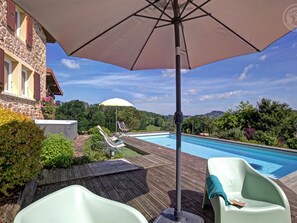 Ein Poolbereich mit Holzterrasse, Liegestühlen und einem großen Sonnenschirm, der Schatten spendet.