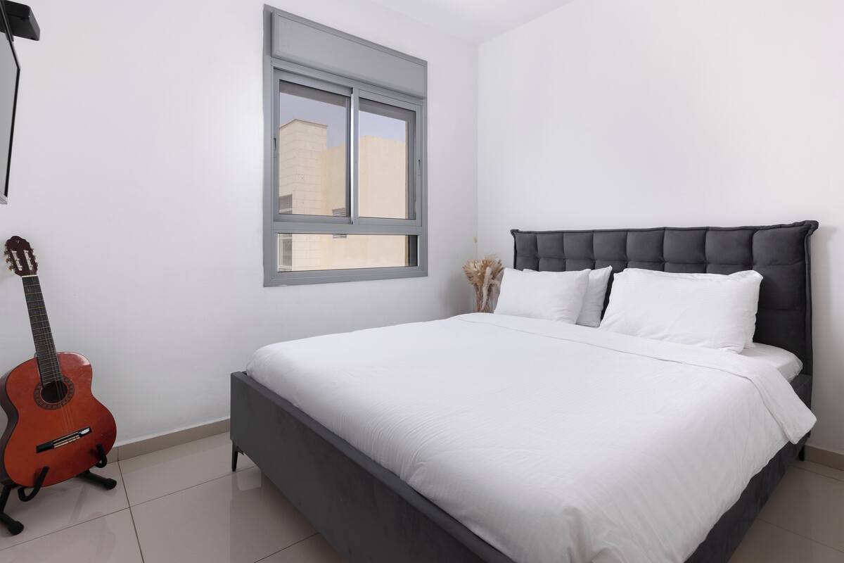A bedroom with a bed, a window, and a guitar.