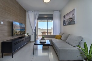 Un salón moderno con televisor de pantalla plana, sofá, mesa de centro y balcón con vista al mar.