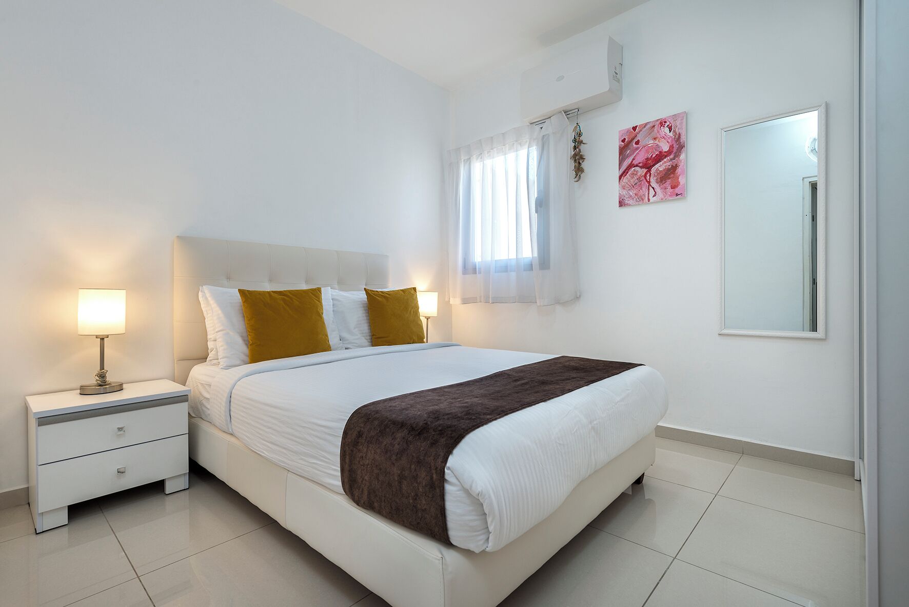 A neatly arranged bedroom with a bed, bedside tables, a lamp, and a mirror.