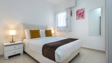 A neatly arranged bedroom with a bed, bedside tables, a lamp, and a mirror.
