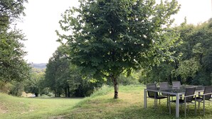 An outdoor dining area with a table and chairs, surrounded by trees and a grassy field. - The house of pech dordogne (Coux-et-Bigaroque-Mouzens)