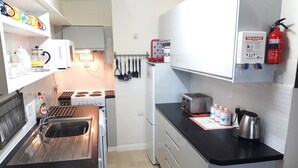 A compact kitchen with a stove, sink, and toaster. There are utensils hanging on the wall, a fire extinguisher, and a fire blanket on the countertop.