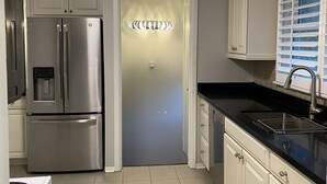 A modern kitchen with white cabinets, stainless steel appliances, a black countertop, and a tiled floor. - "The Cottage at Spruce" Tranquil, Cozy and Rustic (Burlington)