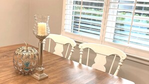 A dining table with a candle and a decorative bowl, white chairs, and a window with blinds. - "The Cottage at Spruce" Tranquil, Cozy and Rustic (Burlington)