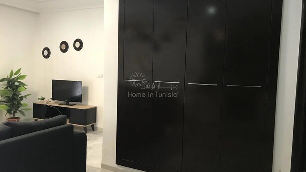 A modern living room with a black wardrobe, a flat-screen TV, a sofa, and a potted plant. - Superb Mont Carlo Hamam Sousse vacation apartment (Hammam Sousse)