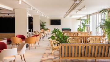 A modern lounge area with seating arrangements, a flat-screen TV, and large windows allowing natural light.