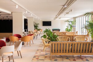 A modern lounge area with seating arrangements, a flat-screen TV, and large windows allowing natural light.