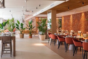 A modern restaurant with indoor seating, potted plants, and a wooden ceiling. - Atzavara Hotel Spa (Santa Susanna)