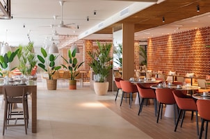 Un restaurante moderno con mesas dentro, plantas en macetas y techo de madera.