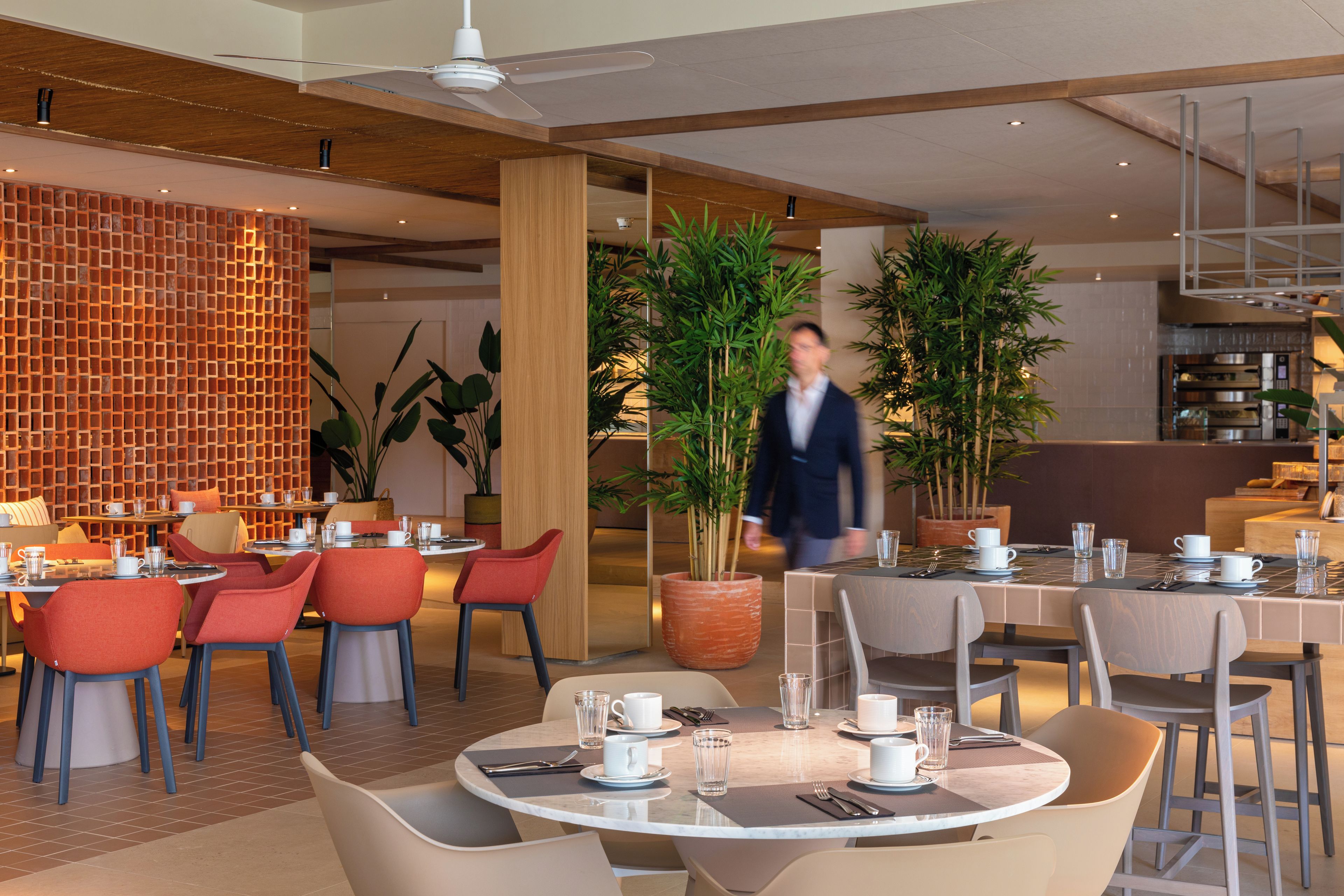 Un interior de restaurante moderno con mesas redondas, sillas y plantas en macetas.