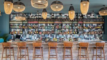 Uma área de bar com várias garrafas de bebidas, banquetas de madeira e luminárias de vime suspensas.
