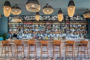 A bar area with multiple liquor bottles, wooden bar stools, and hanging wicker light fixtures. - Atzavara Hotel Spa (Santa Susanna)