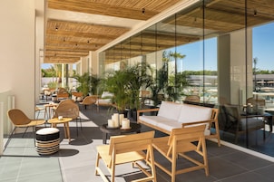 Un área lounge moderna al aire libre con mobiliario de mimbre, un sofá acolchado y plantas en macetas.