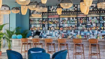 A bar area with multiple hanging light fixtures, a variety of liquor bottles on shelves, and several bar stools.