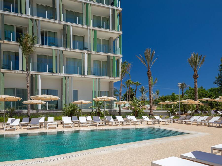 A hotel with a pool area, sun loungers, and umbrellas.