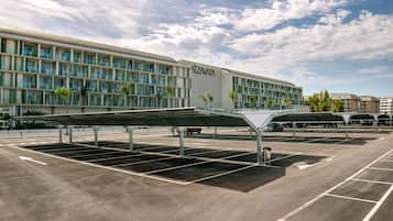 A parking area with covered parking bays in front of a building with a modern design and a sign that reads 'TZAVARA'.