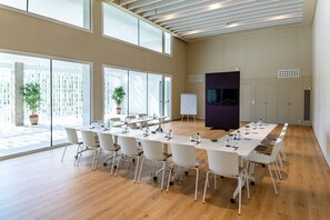 Un salón de conferencias con una larga mesa, sillas, una pizarra y una pantalla de televisión.
