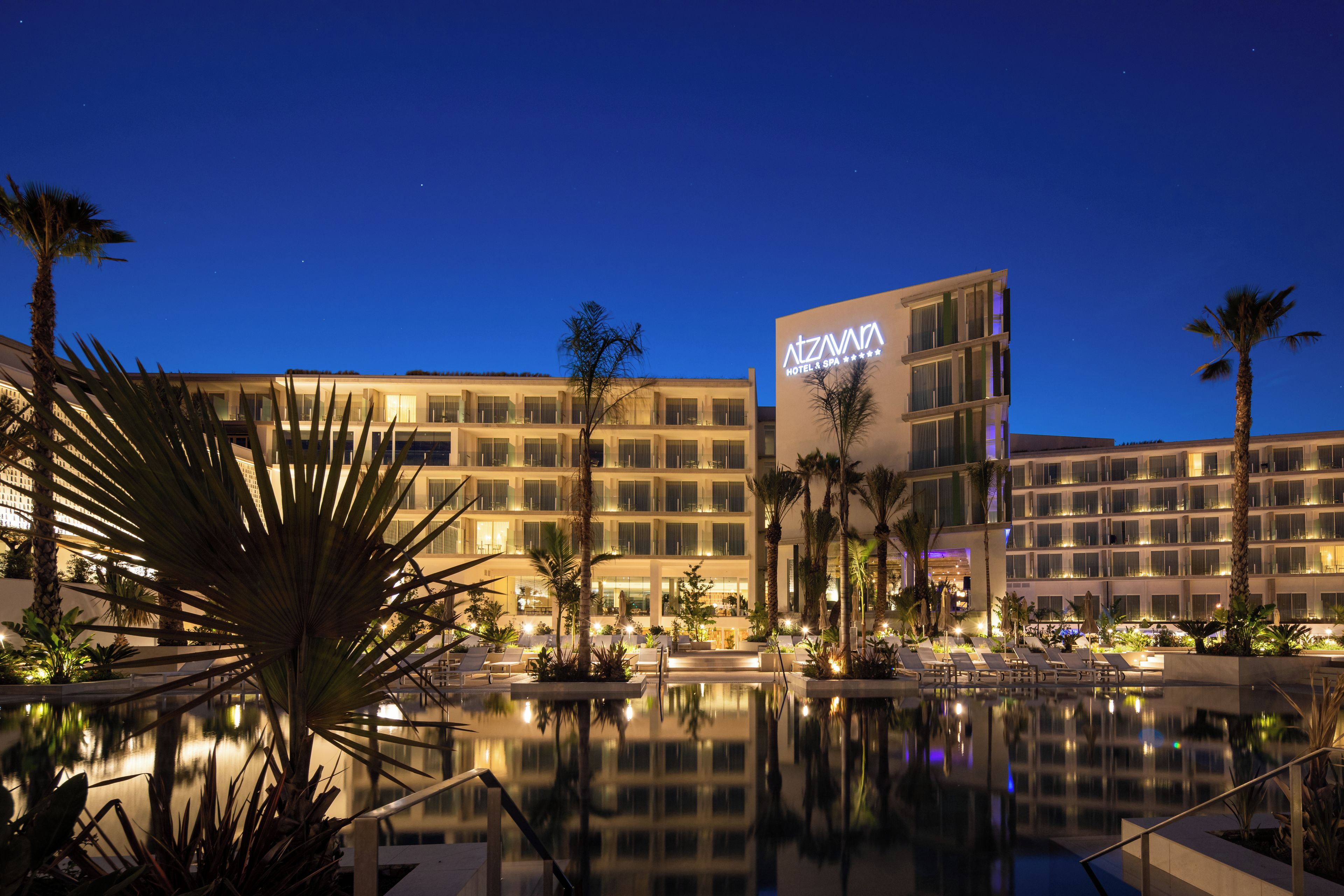 A hotel with a pool, palm trees, and a night sky.