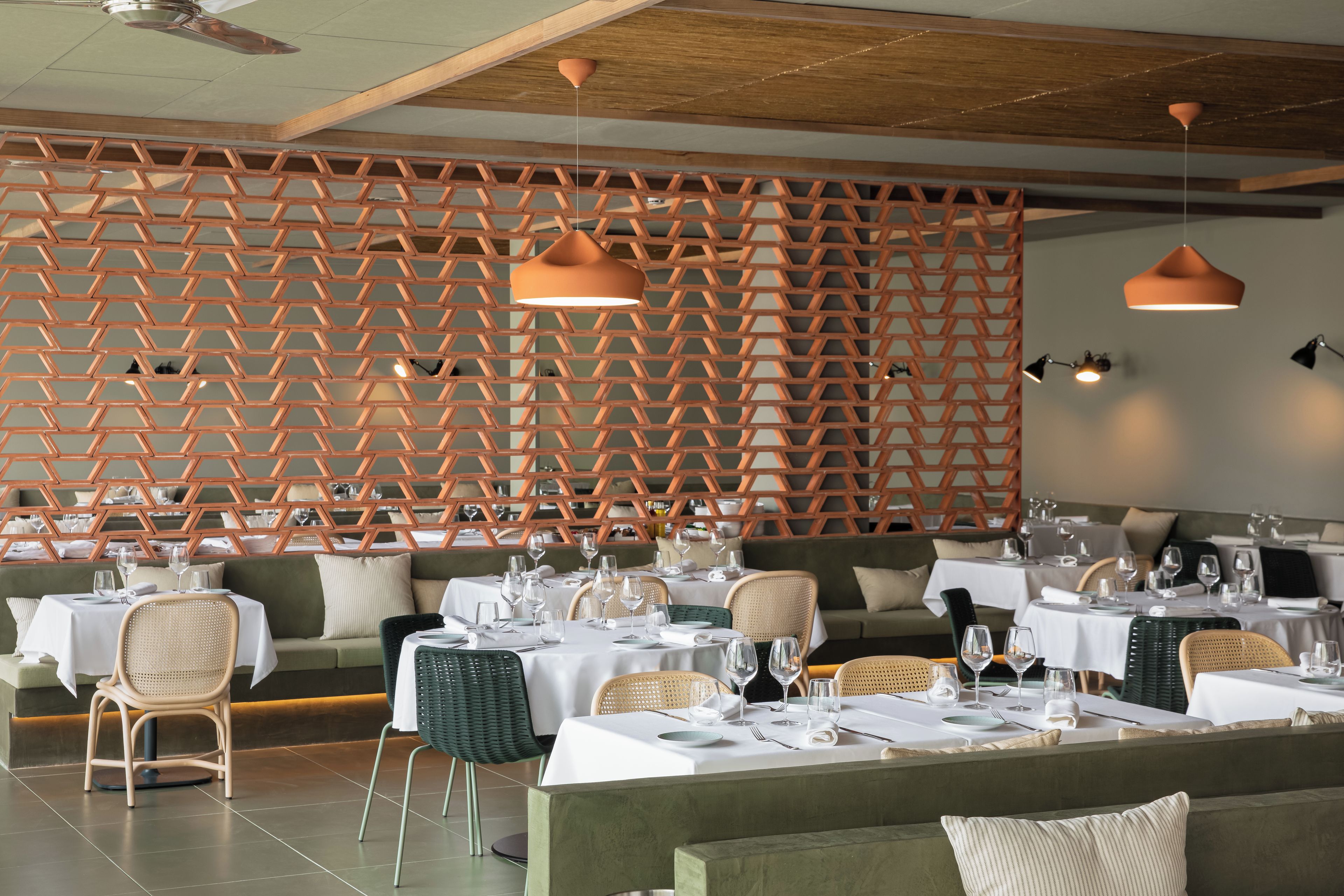 Interior de restaurante con separadores de madera hexagonales, mesas redondas con sillas e iluminación colgante.