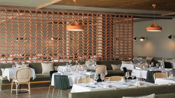Interior de restaurante con separadores de madera hexagonales, mesas redondas con sillas e iluminación colgante.