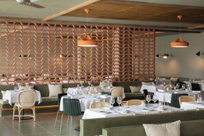 A restaurant interior with hexagonal wooden partitions, round tables with chairs, and pendant lighting. - Atzavara Hotel Spa (Santa Susanna)