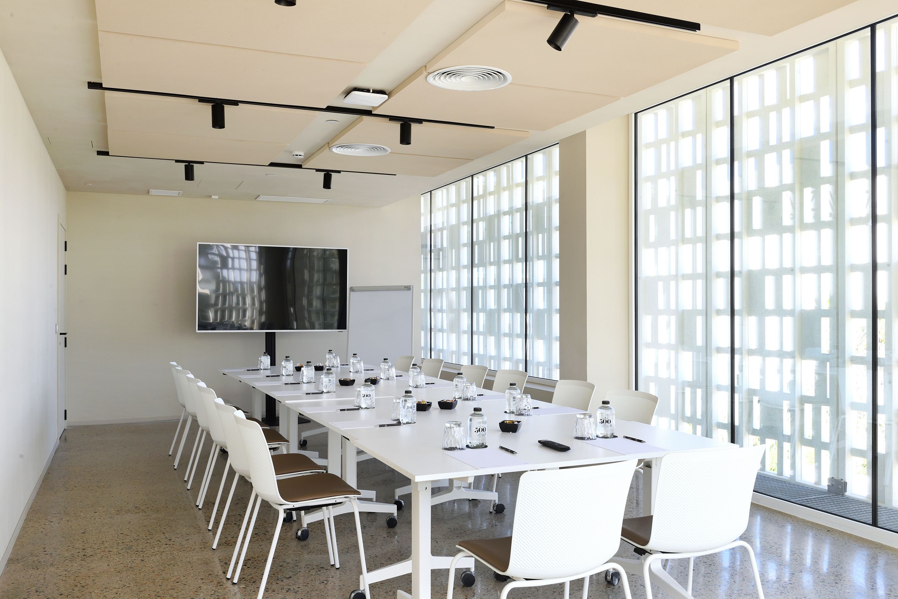A conference room with a long table, white chairs, a whiteboard, and a large window.