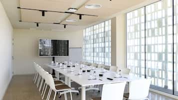 A conference room with a long table, white chairs, a whiteboard, and a large window.