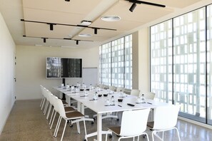 A conference room with a long table, white chairs, a whiteboard, and a large window. - Atzavara Hotel Spa (Santa Susanna)