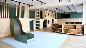 Una sala de juegos con un tobogán, estructuras para escalar y estantes llenos de juguetes.