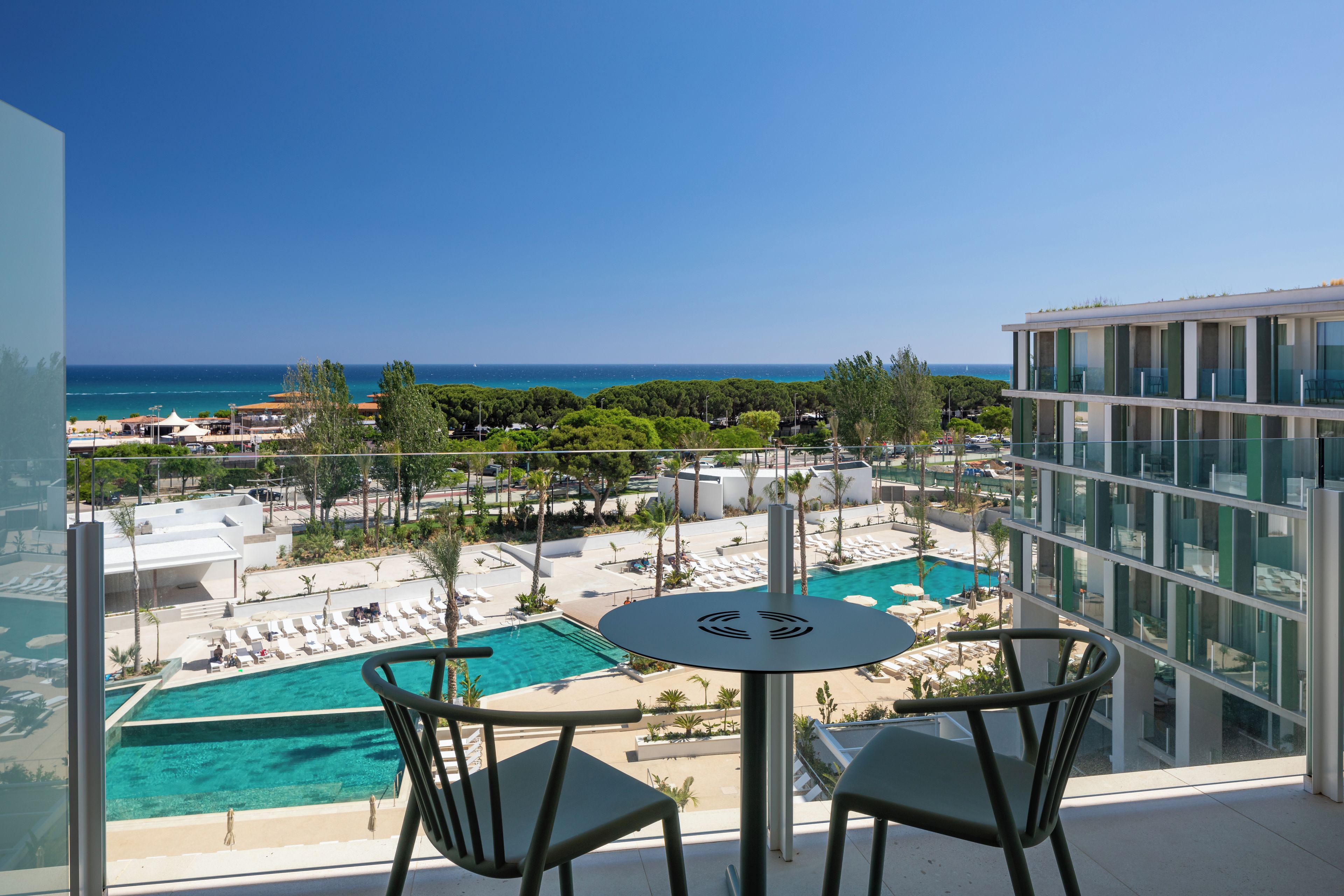 A balcony with a view of a swimming pool and the sea.