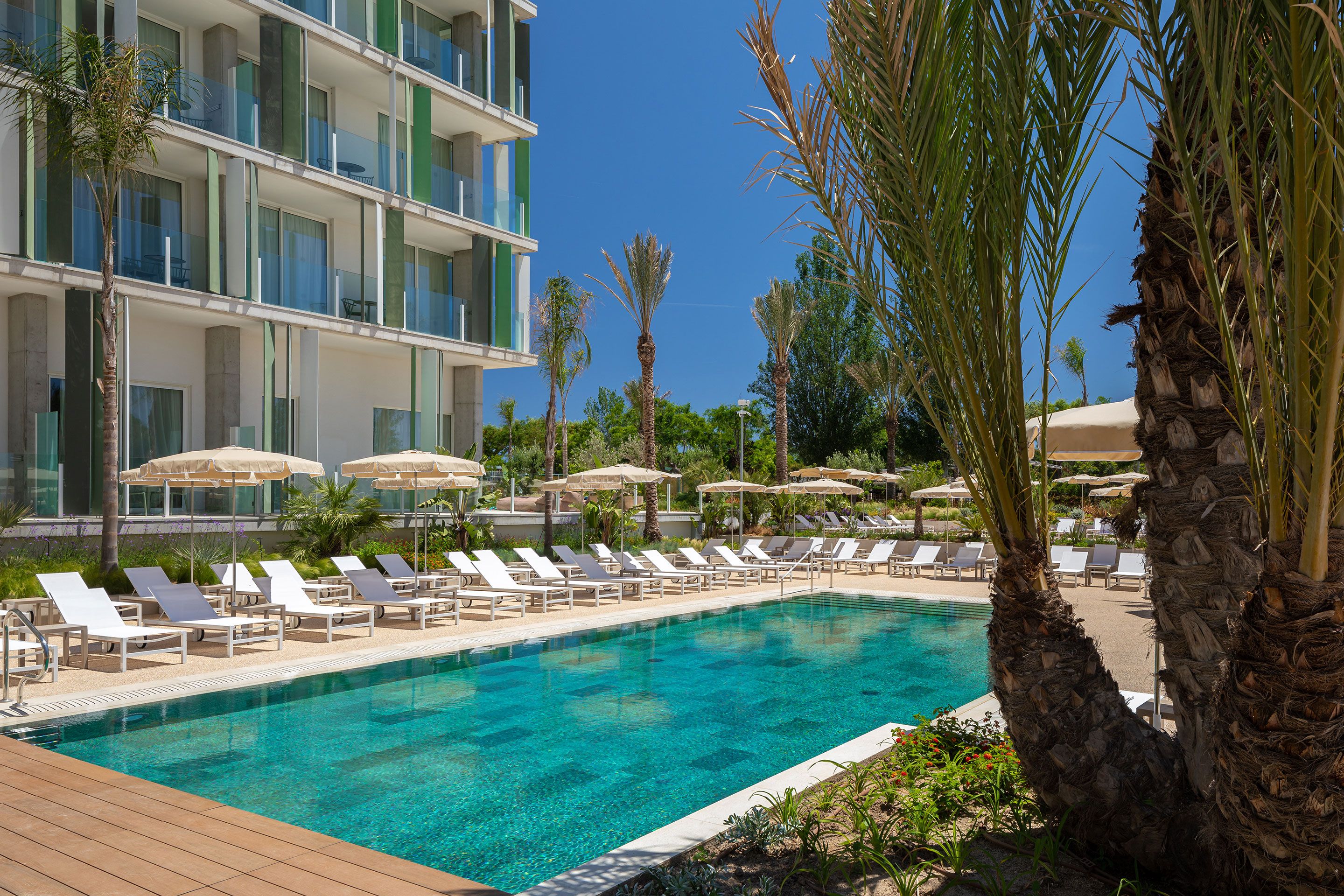 A poolside area with lounge chairs and umbrellas, a clear blue pool, and a modern building with balconies.