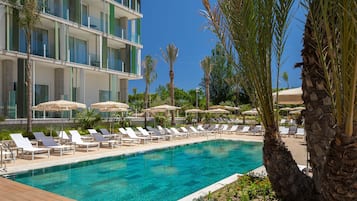 A poolside area with lounge chairs and umbrellas, a clear blue pool, and a modern building with balconies.