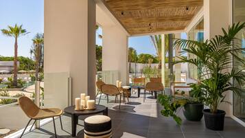 Un área de lounge al aire libre moderna con mobiliario de mimbre, plantas en macetas y una piscina al fondo.