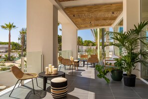A modern outdoor patio with wicker furniture, potted plants, and a view of a pool and palm trees. - Atzavara Hotel Spa (Santa Susanna)