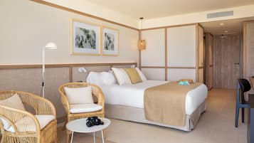 Quarto de hotel com uma cama, duas cadeiras de vime, uma pequena mesa com uma câmera e obras de arte emolduradas na parede.