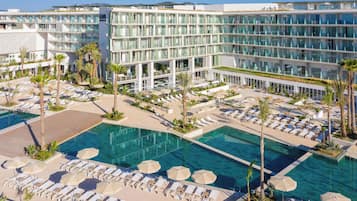 Un hotel con varias piscinas, tumbonas y palmeras.