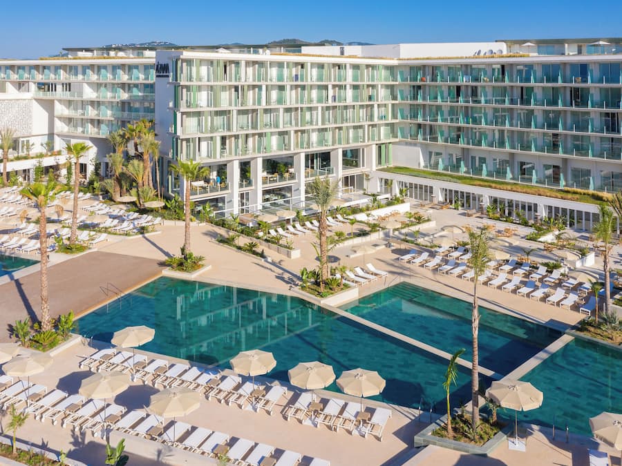 Un hotel con varias piscinas, tumbonas y palmeras.