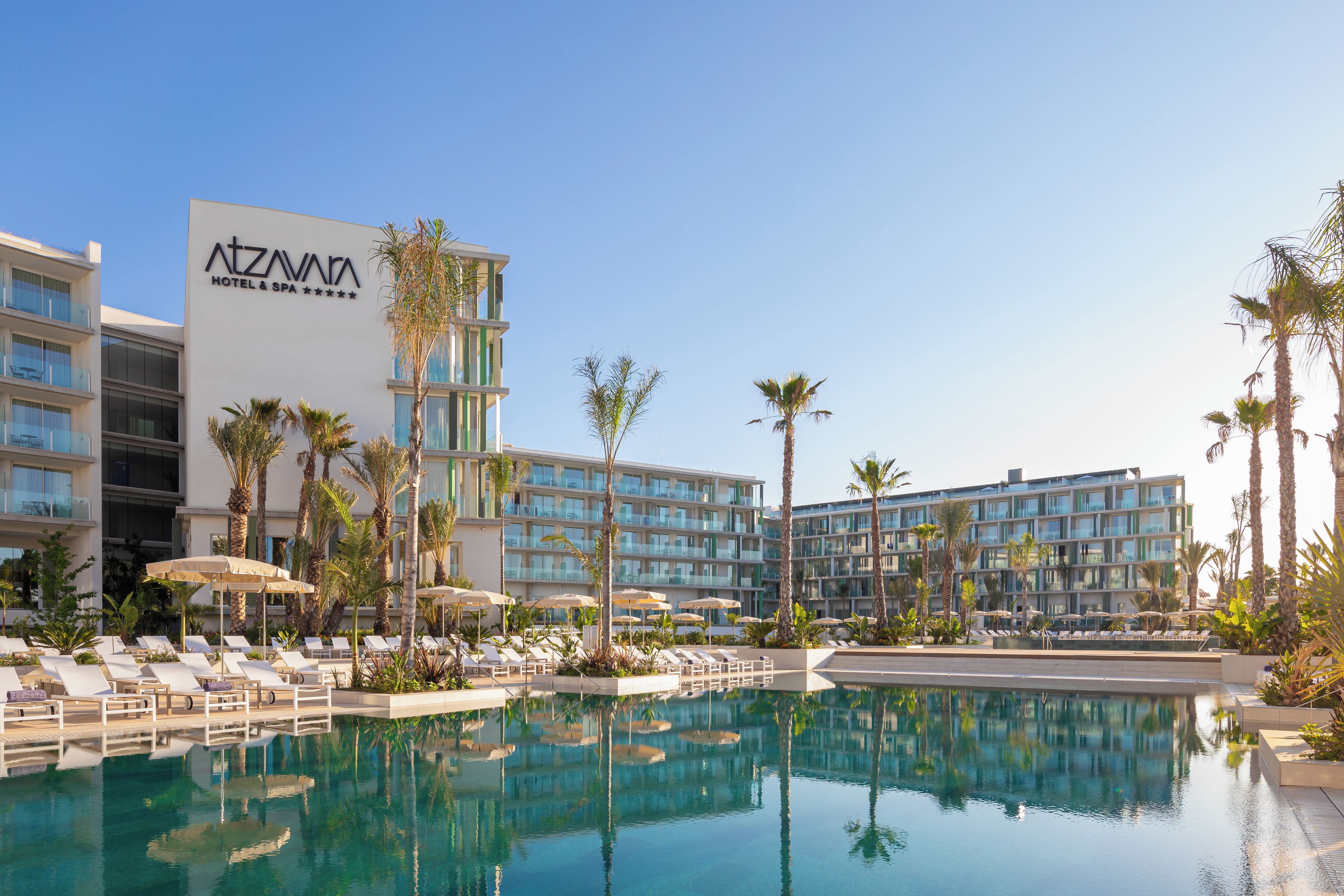 Un hotel con piscina, tumbonas y palmeras.