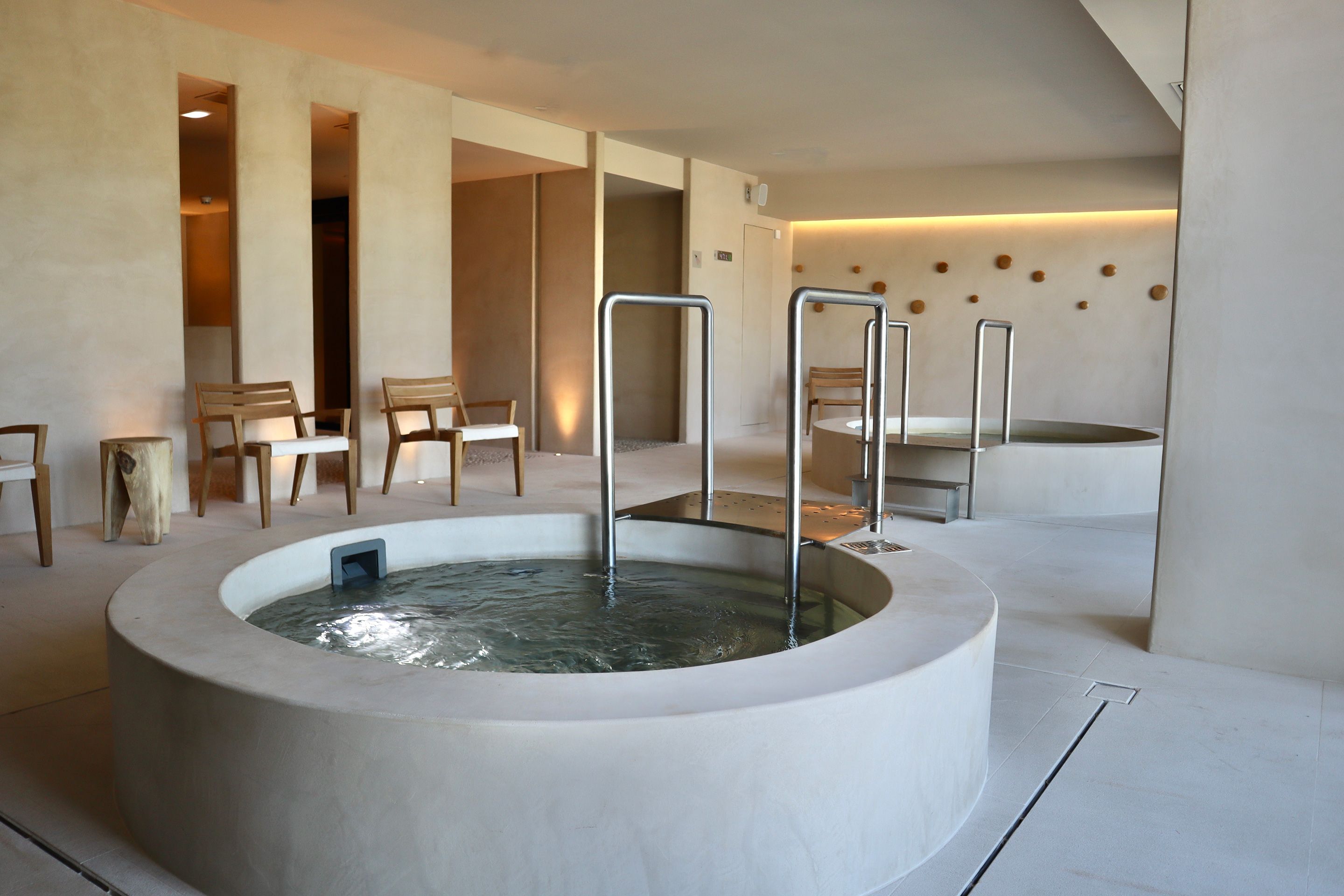 Un espace spa moderne doté d’un grand jacuzzi central, de chaises en bois et d’un design minimaliste.
