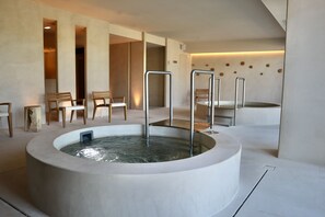 A modern spa area with a central hot tub, wooden chairs, and a minimalist design. - Atzavara Hotel Spa (Santa Susanna)