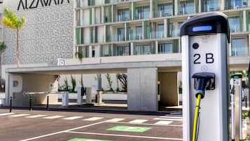Un estacionamiento con estaciones de carga para vehículos eléctricos, un edificio de fachada moderna y un cielo despejado.